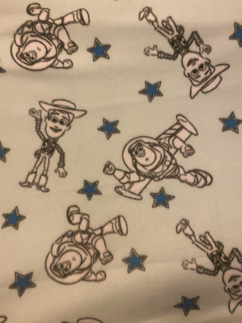 May include: A light blue fabric with a repeating pattern of white outlines of characters from the Toy Story movie. The characters include Woody, Buzz Lightyear, and the alien. The background is dotted with blue stars.