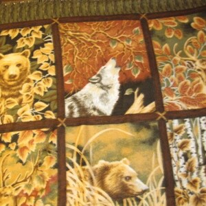 Pode incluir: Uma colcha de retalhos com um tema de floresta. A colcha apresenta imagens de ursos, lobos, veados e &aacute;rvores em tons de marrom, verde e amarelo.