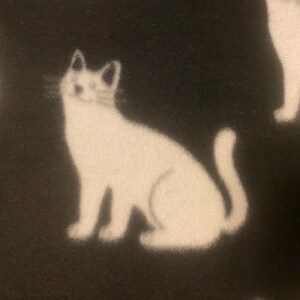May include: Black fabric with a white cat silhouette pattern. The cat is sitting with its tail curled around its body.