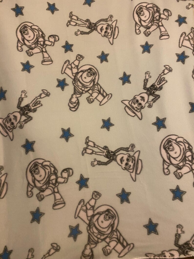 May include: A light blue fabric with a repeating pattern of white cartoon characters and blue stars. The characters are of a space ranger and a cowboy.