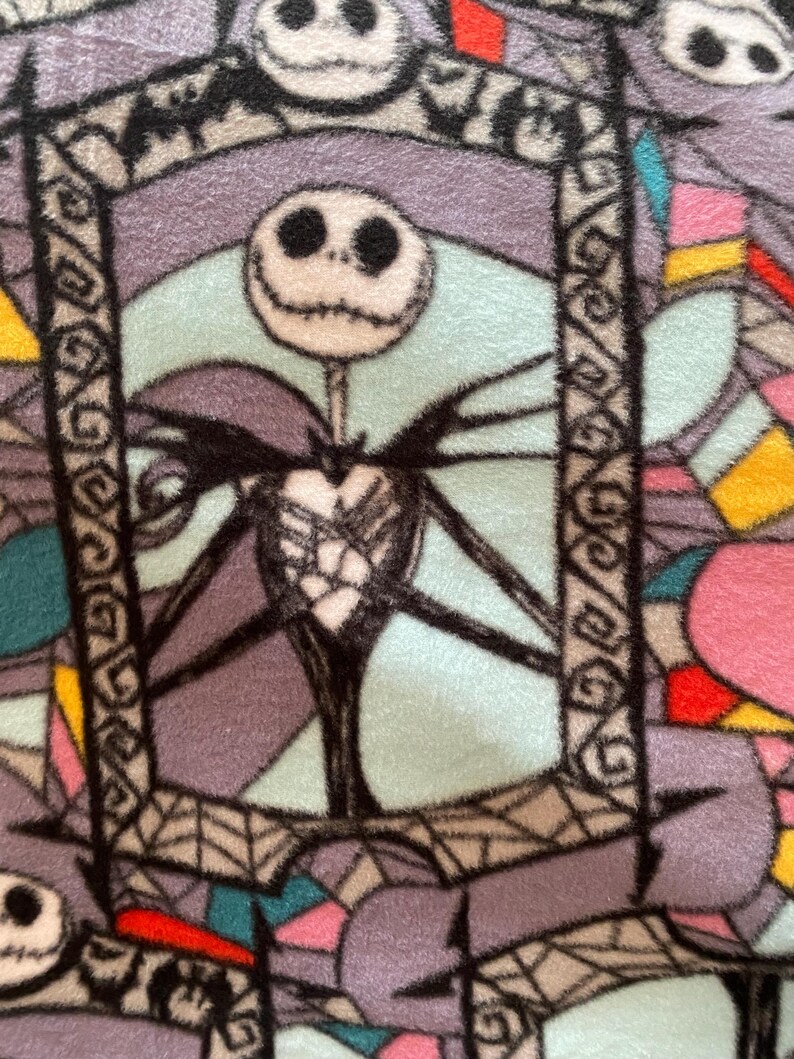 Puede incluir: Un primer plano de una tela con un patr&oacute;n de vitral que presenta a Jack Skellington de Pesadilla antes de Navidad. La tela es una mezcla de morado, azul, rosa, amarillo y rojo.
