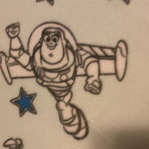May include: A black and white illustration of a cartoon character flying a spaceship. The character is wearing a space suit and has a big smile. The background is light blue with white stars.