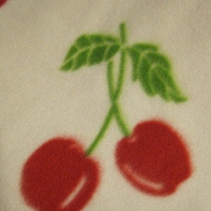 May include: A white background with a red cherry with a green stem and leaf. The cherry is on the right side of the image. There is another red cherry on the left side of the image with a green stem and leaf.
