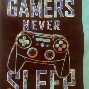 May include: A black and blue throw blanket with the text "GAMERS NEVER SLEEP" and a stylized image of a video game controller.