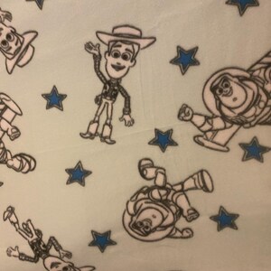 May include: A light blue fabric with a repeating pattern of Woody and Buzz Lightyear from Toy Story. The characters are outlined in black and the background is a light blue color. There are also blue stars scattered throughout the fabric.