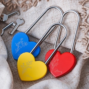 May include: Three heart-shaped padlocks in blue, yellow, and red, with silver bows. Each padlock has a floral design and the name "Jenny" engraved. Three keys are visible in the background.