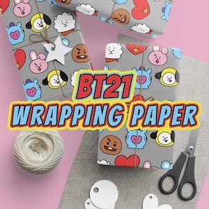 May include: Gray wrapping paper featuring a repeating pattern of colorful BT21 character faces, tied with brown twine and a white star-shaped gift tag. The text BT21 WRAPPING PAPER is overlaid in large, bold, yellow and blue outlined letters.