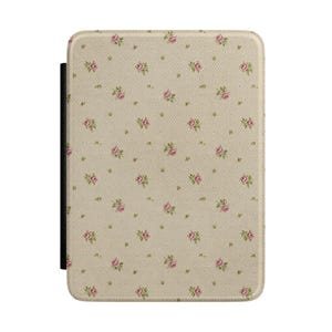 Puede incluir: Una funda protectora rectangular para lector electrónico con fondo beige claro y un patrón repetitivo de pequeñas flores de rosa rosadas y diminutas hojas verdes. La funda tiene una superficie texturizada y un lomo negro a la izquierda.