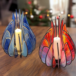 May include: Three decorative candle holders with a stained glass effect. The holders feature a petal-like design in shades of blue, red, and orange, with a gold trim. Each holder contains a white candle. The holders are on a wooden surface.