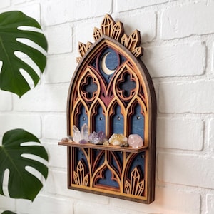May include: A wall-mounted wooden shelf featuring a gothic arch design with layered cutouts, a crescent moon, and star motifs. The structure is finished in dark wood tones and holds a collection of various raw crystals on a horizontal ledge.