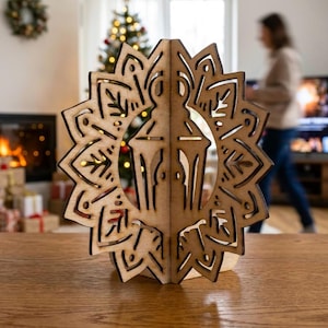 May include: A laser-cut wooden ornament featuring a central lantern shape surrounded by a geometric, star-like mandala pattern. The light brown wood has dark, charred edges from the cutting process, creating a three-dimensional structure.