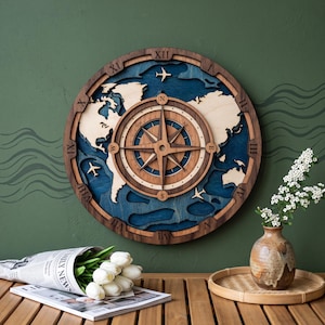 May include: A circular wooden wall clock featuring a layered world map design in light wood and blue tones. The center displays a compass rose, while the outer frame is marked with Roman numerals. Small airplane silhouettes are placed on the map.