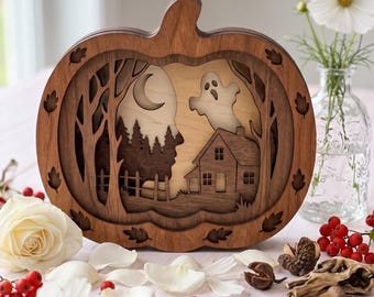 May include: A layered wooden pumpkin-shaped decoration featuring a cutout scene of a house, trees, a crescent moon, and a ghost. The dark brown wood frame is accented with leaf cutouts, while the interior layers show a lighter wood background.