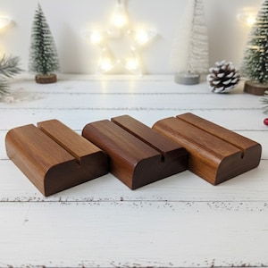 May include: Three wooden display stands with a slot for holding items. The stands are made of dark brown wood with a smooth finish. The background includes Christmas decorations, such as small trees and a star-shaped light.