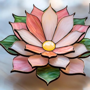 Könnte beinhalten: Glasmalerei-Lotusblume mit rosa, pfirsichfarbenen, weißen und grünen Blütenblättern. Die Blume hat eine gelbe Mitte und ist schwarz umrandet. Ein kleines Symbol befindet sich in der oberen rechten Ecke.