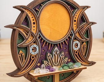 May include: A circular layered wooden wall art piece featuring a central sun, flanking crescent moons, and a small shelf holding various raw crystals. The design incorporates deep purple, green, and natural wood tones with intricate cutouts.