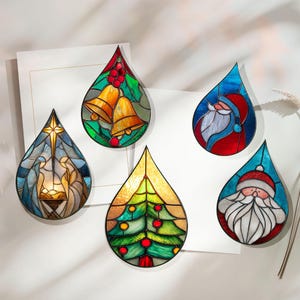 May include: Five stained glass Christmas ornaments in a teardrop shape. Designs include a nativity scene, bells, a Christmas tree, and two Santa Claus figures. The ornaments feature vibrant colors and intricate details, perfect for holiday decor.