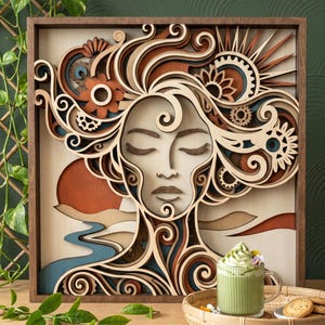 Puede incluir: Una pieza de arte mural de madera multicapa que presenta un rostro estilizado con cabello fluido integrado con engranajes mecánicos, elementos florales y un paisaje de atardecer. La obra está enmarcada en madera oscura con tonos crema, marrón y azul.