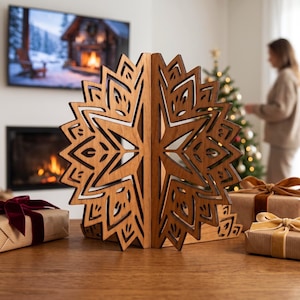 Könnte beinhalten: Ein Paar lasergeschnittene Buchstützen aus Holz mit einem symmetrischen Stern- oder Schneeflockenmuster und komplizierten geometrischen Ausschnitten. Die natürliche braune Holzmaserung ist sichtbar und beide Teile bilden ein Kreisdesign.