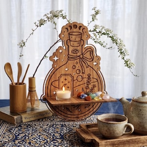 May include: A laser-cut wooden wall shelf shaped like a potion bottle, featuring engraved designs of an eye, stars, bubbles, and a sprig of lavender. The shelf holds a small white tea light candle and a collection of colorful polished gemstones.