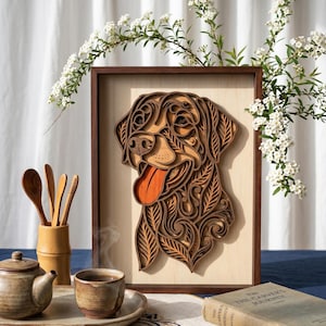 Puede incluir: Una pieza de arte mural de madera multicapa que presenta un retrato de perro estilizado con intrincados recortes de hojas y espirales. La obra está enmarcada en madera oscura y muestra varios tonos de marrón y bronceado con una lengua naranja brillante.