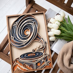May include: A multi-layered wooden wall art piece featuring a record player where the turntable and horn are stylized as a swirling galaxy with planets and a sun. The design uses shades of dark blue, light wood, and orange in a rectangular frame.
