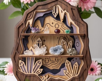 May include: A multi-layered wooden display shelf shaped like a cave, featuring two horizontal shelves holding various raw crystals. The frame is constructed from dark and light wood, with laser-cut crystal motifs and engraved star patterns on the back panel.