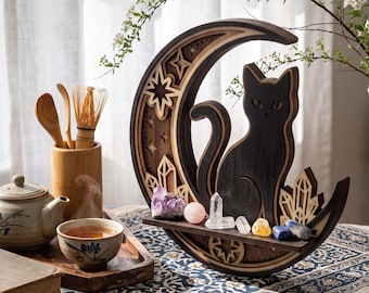May include: A crescent moon-shaped wooden shelf featuring a dark silhouette of a cat sitting in the center. The shelf is decorated with star cutouts and holds a collection of various raw and polished crystals, including amethyst and clear quartz.
