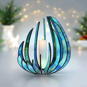May include: A decorative candle holder with a stained glass design. The holder features blue and green glass panels arranged in a stylized floral shape. A white candle is lit inside the holder, casting a warm glow. The holder is approximately 6 inches tall.