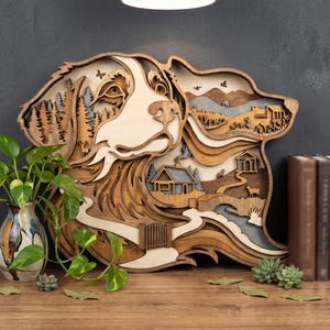 May include: A multi-layered wooden wall art piece shaped like a dog head, featuring intricate laser-cut scenes of a forest, a cabin, a winding path, and wildlife. The design uses various shades of natural wood tones to create depth and texture.