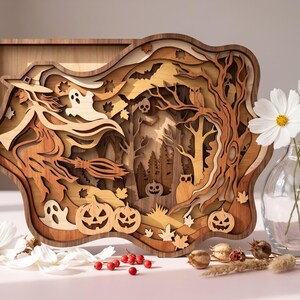 May include: A multi-layered wooden wall art piece featuring a witch on a broomstick, ghosts, pumpkins, owls, and a forest scene. The design uses various shades of natural wood to create depth, with intricate cutouts of bats and autumn leaves.