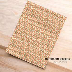 May include: A rectangular sheet with a repeating pattern of orange fruit and green leaves on a cream background. The text "dandelion designs" and "clay transfer sheets" are printed in black. The sheet is on a light brown wooden surface.