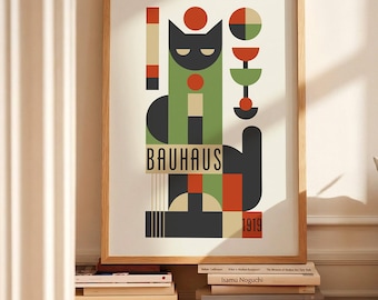 May include: A framed Bauhaus art print featuring a geometric cat design in green, black, red, and beige. The word "BAUHAUS" is printed below the cat, with "1919" at the bottom. The print is in a light wood frame and rests on a stack of books.