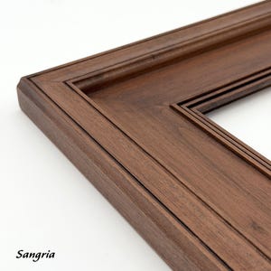May include: Close-up of a dark brown wooden picture frame corner. The frame has a detailed, layered design with a beveled edge. The word "Sangria" is printed in the bottom left corner.