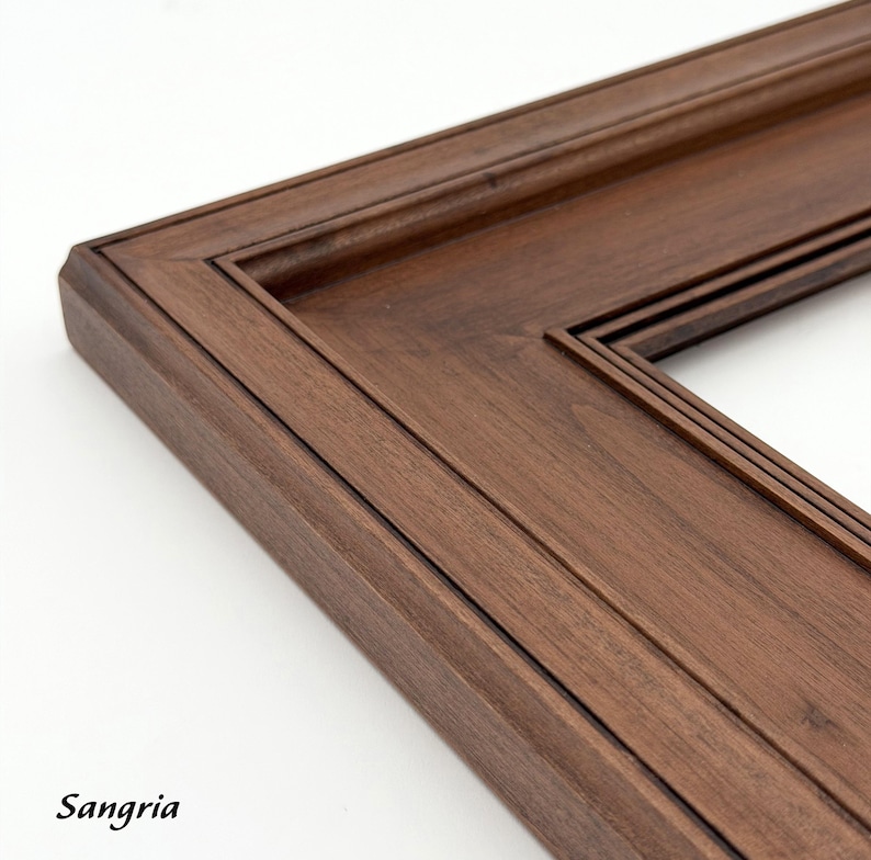 May include: Close-up of a dark brown wooden picture frame corner. The frame has a detailed, layered design with a beveled edge. The word "Sangria" is printed in the bottom left corner.