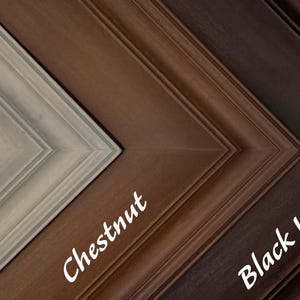 May include: Close-up of four wooden picture frame samples in a diagonal arrangement. The frames are labeled "Graywash", "Chestnut", and "Black Walnut". The frames have a beveled edge and are in shades of gray, brown, and black.