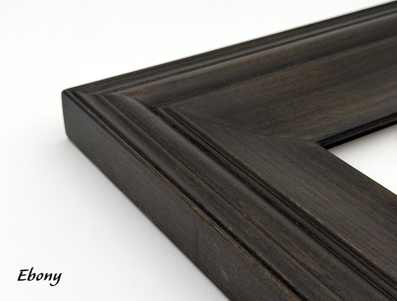 May include: Close-up of a dark ebony-colored picture frame corner. The frame has a beveled edge and a detailed, textured surface. The word "Ebony" is printed in a cursive font in the lower left corner. The frame is likely made of wood.