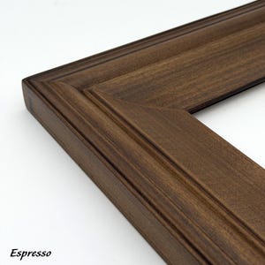 May include: Close-up of a corner of a wooden picture frame in a rich espresso color. The frame has a detailed, grooved design and a beveled edge. The word "Espresso" is printed in the bottom left corner.