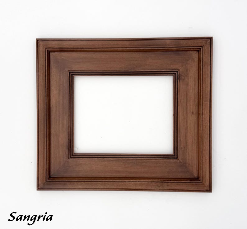 May include: A rectangular wooden picture frame with a dark brown finish. The frame has a double-layered design with a recessed inner edge. The word "Sangria" is written in black script at the bottom.