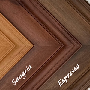 May include: Close-up of three wooden picture frames in shades of honey, sangria, and espresso. The frames are angled, showcasing their detailed molding and color variations. The names of the colors are written on the frames.
