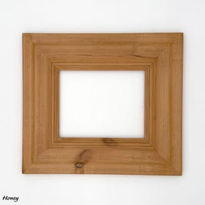 May include: A rectangular wooden picture frame with a honey-colored finish. The frame has a beveled edge and a visible wood grain. The frame is designed to hold a rectangular image. The word "Honey" is written in the bottom left corner.