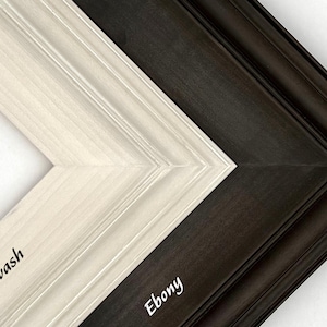 May include: Close-up of two wooden picture frame corners. One is whitewashed, the other is ebony. The whitewash frame has the word "Whitewash" printed on it. The ebony frame has the word "Ebony" printed on it.
