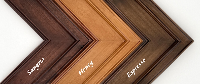 May include: Close-up of three wooden picture frames in a V-shape, showcasing different stain colors. The colors are Sangria, Honey, and Espresso, with the names of the colors written in white script on each frame.