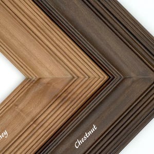 May include: Close-up of two wooden picture frame samples in honey and chestnut colors. The frames have a grooved design and are angled to show the different colors. The word "Honey" is written on the honey-colored frame, and "Chestnut" is written on the chestnut-colored frame.