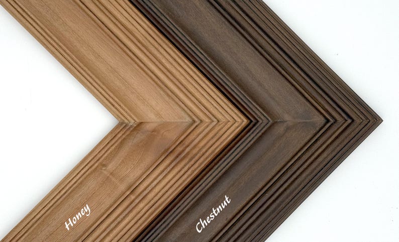 May include: Close-up of two wooden picture frame samples in honey and chestnut colors. The frames have a grooved design and are angled to show the different colors. The word "Honey" is written on the honey-colored frame, and "Chestnut" is written on the chestnut-colored frame.