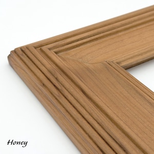 May include: Close-up of a corner of a wooden picture frame. The frame is a warm honey color with a grooved design. The word "Honey" is written in black cursive in the bottom left corner.