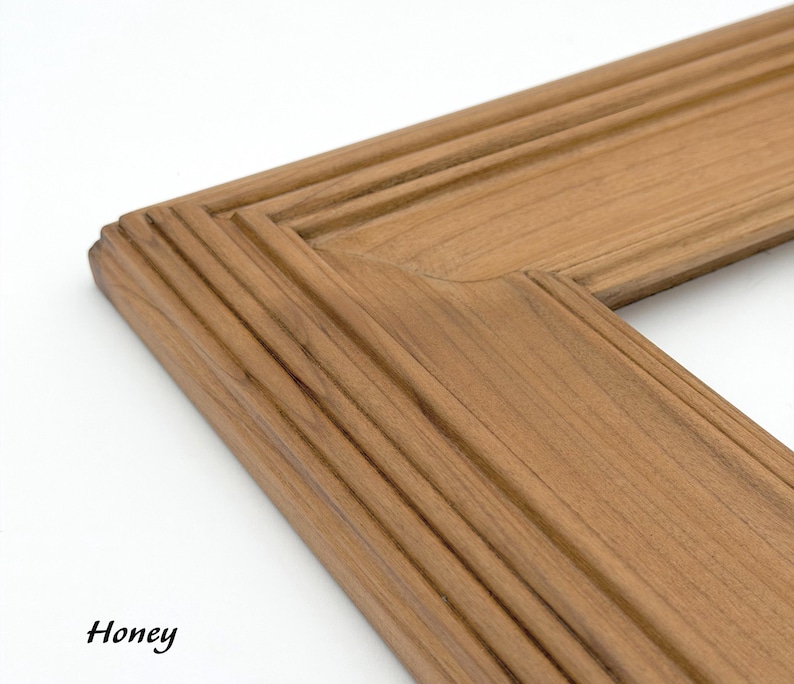 May include: Close-up of a corner of a wooden picture frame. The frame is a warm honey color with a grooved design. The word "Honey" is written in black cursive in the bottom left corner.