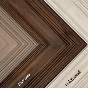 May include: Close-up of three wooden picture frames in different colors: Driftwood, Espresso, and Whitewash. The frames have a textured, grooved design and are angled to show their corners. The names of the colors are written on the frames.