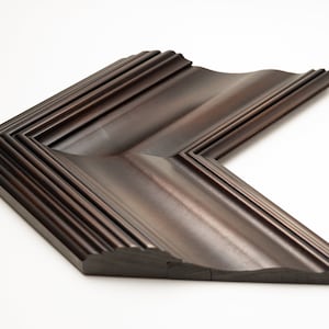 May include: A dark brown wooden picture frame with a decorative, layered, and slightly curved design. The frame is made of wood and has a smooth finish.