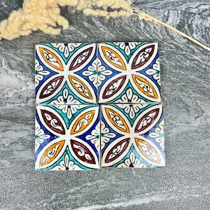 Puede incluir: Cuatro baldosas de cerámica cuadradas con un diseño floral. Las baldosas presentan un patrón simétrico con colores azul, blanco, amarillo, turquesa y granate. Las baldosas están dispuestas en forma cuadrada.